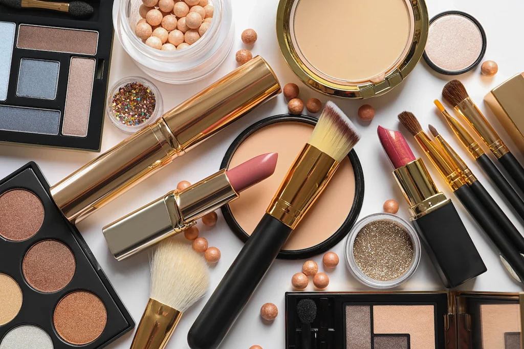 A flat lay of cosmetics: eyeshadow palettes, lipsticks, compact powder, loose pigment and a set of makeup brushes.