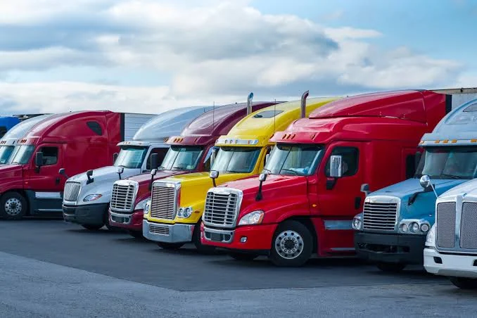 A row of parked long-haul trucks at a logistics yard under a cloudy sky.